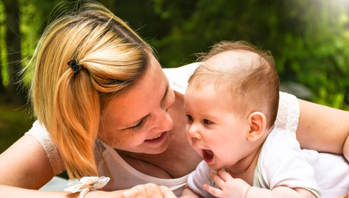 A mom smiles as she plays with her baby on a blanket