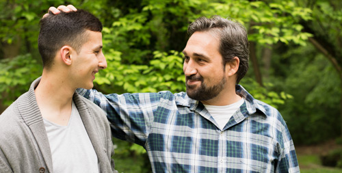 A middle-aged father puts his hand on his son's head as they talk and laugh